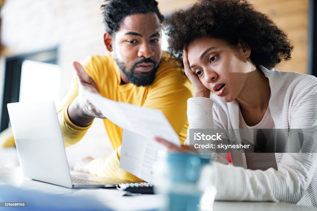 Young black couple having problems with online banking at home. Young African American couple feeling frustrated while paying their bills over laptop at home. Focus is on woman. Financial Bill Stock Photo