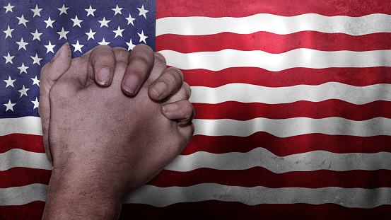 A hand praying with Flag of USA as background. Grunge, depressing look. Can represent adversity, crisis, Christian or Catholic prayer, forgiveness, worship or plea in country. 3d illustration