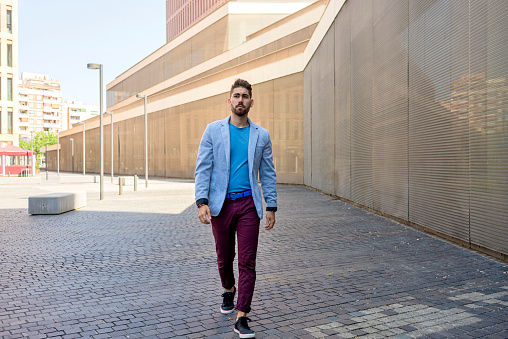 Young bearded man, model of fashion, in urban background wearing casual clothes while walking with hands on pocket