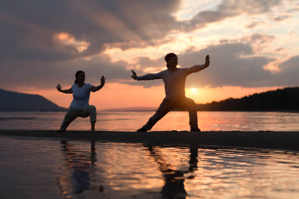 homme et femme faisant le chuan de tai chi au coucher du soleil sur la plage.  activités de plein air en solo. distanciation sociale. concept de mode de vie sain. - tai chi photos et images de collection