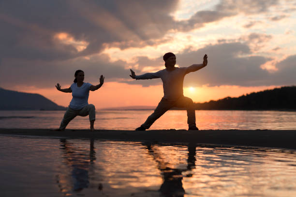 Man and woman doing Tai Chi chuan at sunset on the beach.  solo outdoor activities. Social Distancing. Healthy lifestyle  concept. stock photo