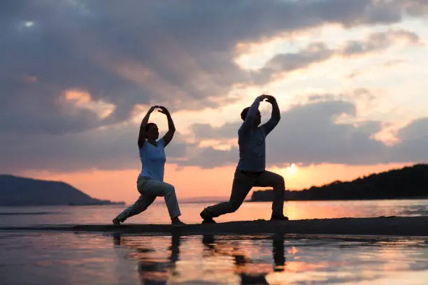 Photo of Man and woman doing Tai Chi chuan at sunset on the beach.  solo outdoor activities. Social Distancing. Healthy lifestyle  concept.