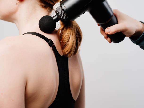woman uses a massage gun. medical-sports device. woman uses massage gun. medical-sports device helps to reduce muscle pain after training, helps to relieve fatigue, affects problem areas of body, improves condition of skin. percussion instrument stock pictures, royalty-free photos & images