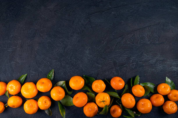 istock Orange tangerines with green leaves on a black stone background. View from above. Copy space 1296494362