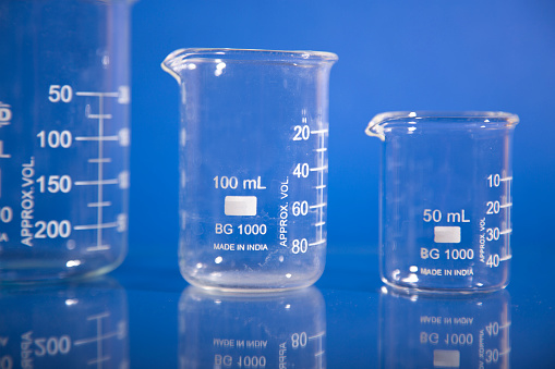 Beakers used in science laboratories on blue background.  Their reflections can be seen in the table where they sit.