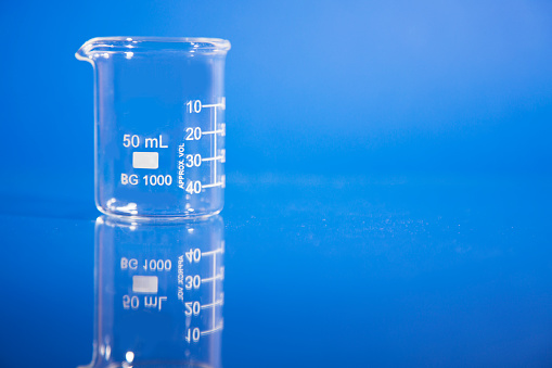 Beakers used in science laboratories on blue background.  Their reflections can be seen in the table where they sit.