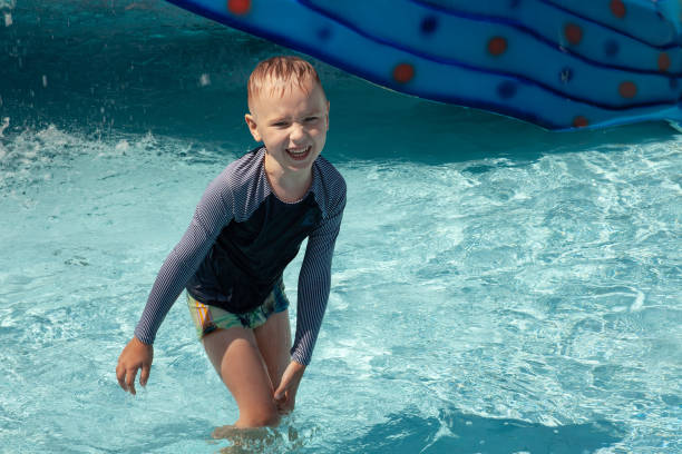 little caucasian boy with blond hair laughing in the middle of children pool. trickles of water everywhere, wet t-shirt and pants, aquamarine colors. - happy kid flash imagens e fotografias de stock