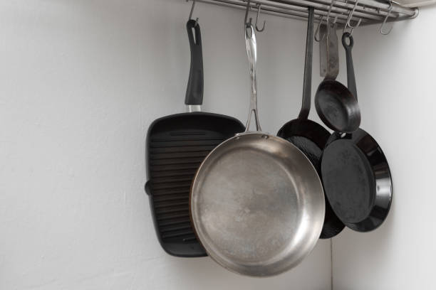 istock Various pans in different sizes and forms for cooking and frying hanging on metal hooks from shelf in kitchen with white wall in background 1296503395