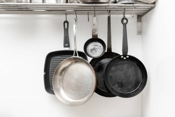 istock Various pans in different sizes and forms for cooking and frying hanging on metal hooks from shelf in kitchen with white wall in background 1296503416