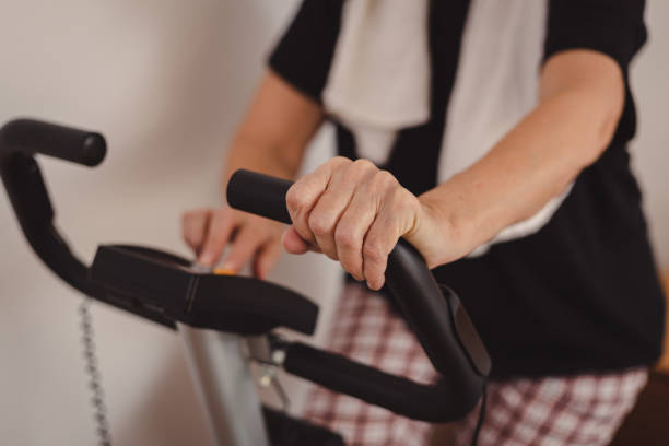 exercice aîné de femme sur le vélo stationnaire à la maison - mature adult home interior chair contemporary photos et images de collection