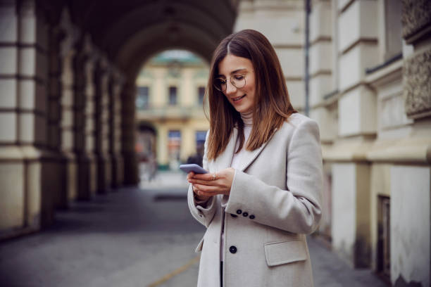 istock Smiling young brunette standing on the street and using phone for texting or hanging on social media. 1296512785