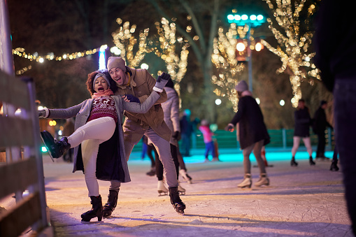 A young girl falling down at ice rink on a beautiful magical night with her boyfriend. Skating, closeness, love, together