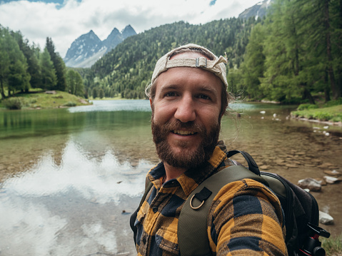Man by the lakeshore takes selfie photo in nature, beautiful mountain lake in Switzerland