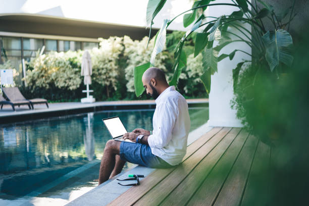 istock Skilled businessman using mockup laptop for making online ticketing and banking during resort recreation on Bali island, Middle Eastern digital nomad connecting to villa wifi on blank netbook 1296521164