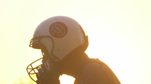 A football player puts on his helmet in sunset