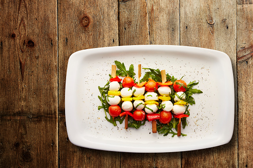 Directly above shot of Tomato, pepper and mozzarella skewers on a bed of dressed Rocket served in a plate