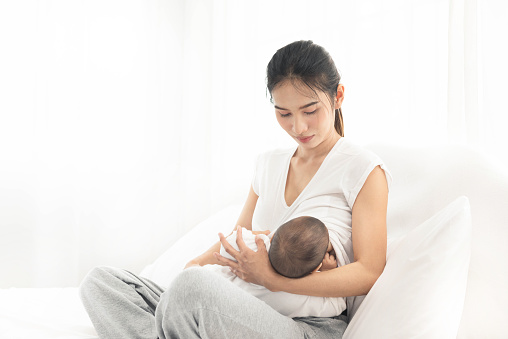 Mother breastfeeding her newborn baby boy. Realistic home portrait