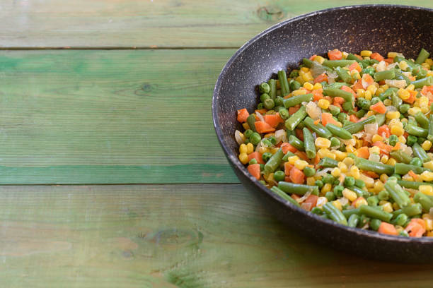 Mix on vegetables fried in the pan on wooden background. Copy space. Healthy food concept.