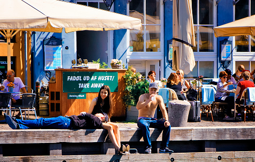 People relaxing the the canal side of Nyhavn, Copenhagen. The green sign says Beer take away and breastfeeding allowed.