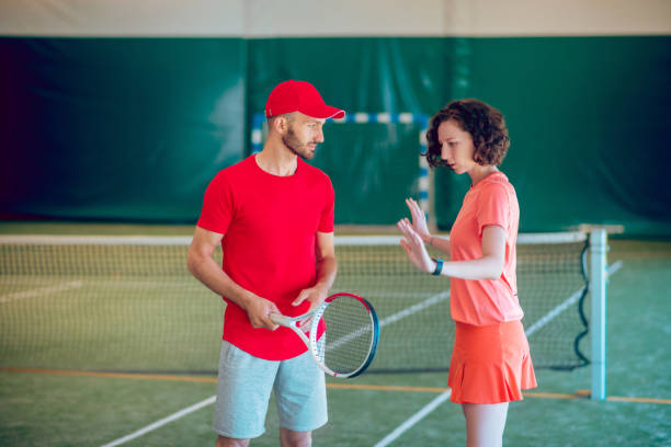 Man in a red cap and with a racket having a workout with his coach