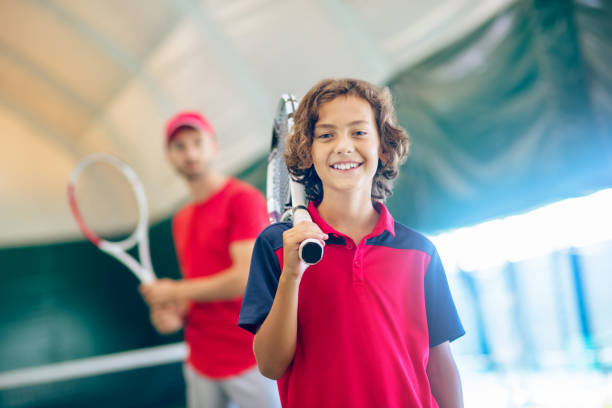 Dark-haired boy standing with a tennis racket and smiling