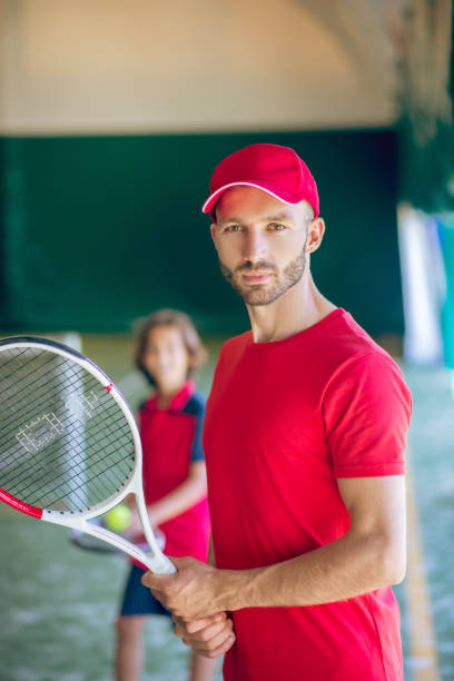 istock Young bearded man in a red cap standing with a tennis racket 1296538944