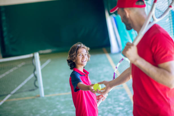 istock Young bearded man in a red cap shaking hands with a dark-haired boy before playing tennis 1296538967