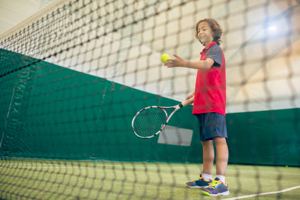 テニスボールを打つ準備ができている赤いtシャツを着た黒髪の少年 - indoor tennis ストックフォトと画像