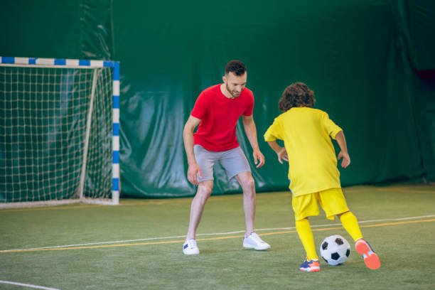 istock Boy in yellow uniform playing soccer with his coach and looking involved 1296539013