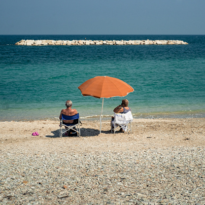 09-12-2016, Fano, Marche, Italy. Elderly couple sunbathes sitting in front of the sea with a parasol
