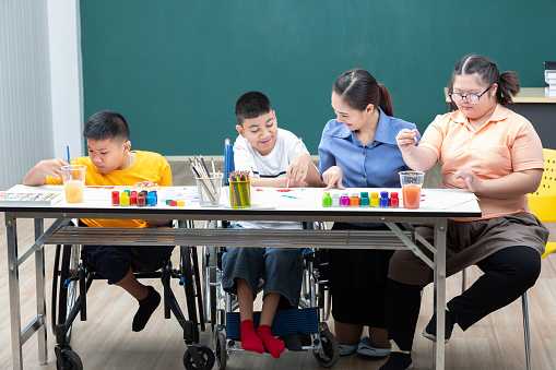 asian group of disabled kids or autism child learning and painting at paper with teacher helping in classroom