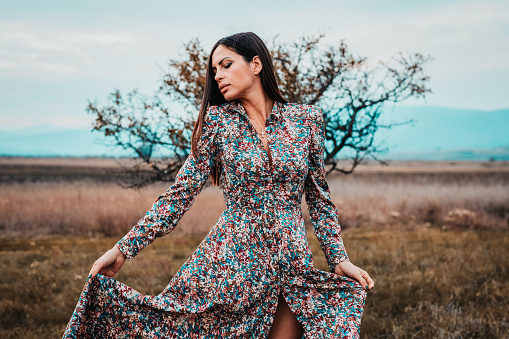 Portrait of a beautiful young woman with long brown hair wearing longsleeved floral pattern dress in nature on a lovely autumn day