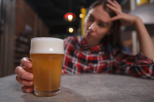 Upset lonely woman holding beer glass, drinking at the pub