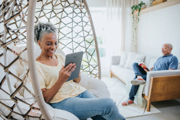 リビングルームのシニアカップル、電子タブレットを使用して読書本と女性 - senior adult relaxation sofa reading ストックフォトと画像