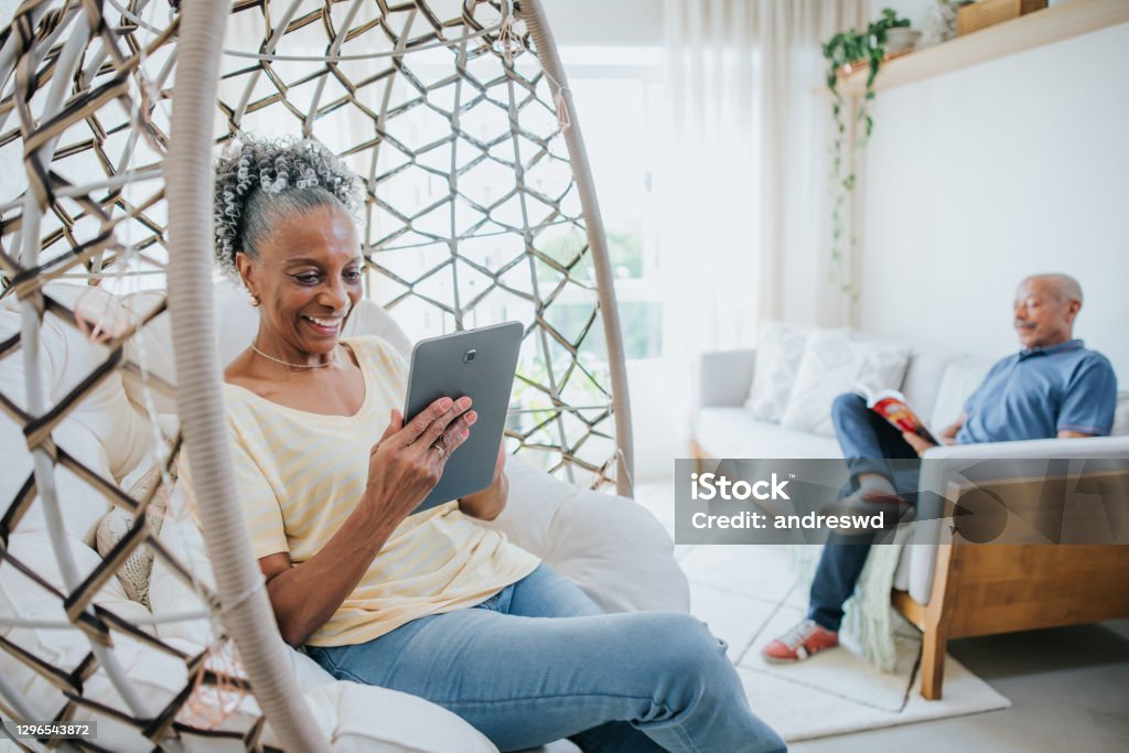 Senior couple in living room, man reading book and woman using digital tablet Senior Adult Stock Photo