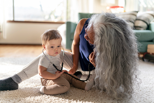 An adorable mixed race baby girl uses a stethoscope while playing make believe with her loving grandmother.