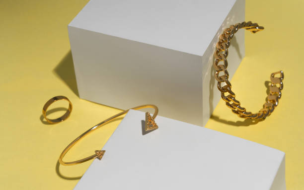 istock Modern golden arrow shape and chain shape bracelets and ring on yellow background 1296551752