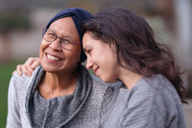 Beautiful Hawaiian senior woman with cancer embracing her adult daughter A senior woman with cancer is embraced and comforted by her adult daughter as they sit outside on a fall evening. The mother is smiling and laughing while the daughter is squeezing her mother affectionately and smiling as well. cancer illness stock pictures, royalty-free photos & images