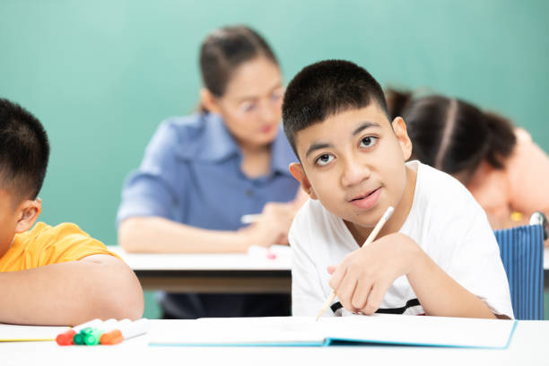 교실에서 돕는 교사가 책상에서 보고 쓰는 아시아 장애인 어린이 또는 자폐증 아동 - physical impairment learning education down syndrome 뉴스 사진 이미지