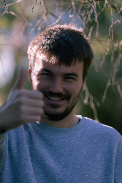 istock Young handsome man with beard wearing casual sweater standing over field approving doing positive gesture with hand, thumbs up smiling and happy for success. Winner gesture. 1296553583