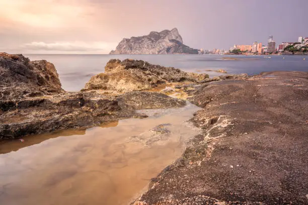 View of the Rock of Ifach from the beach with some rocks in the foreground in Calp, Valencian Community, Spain