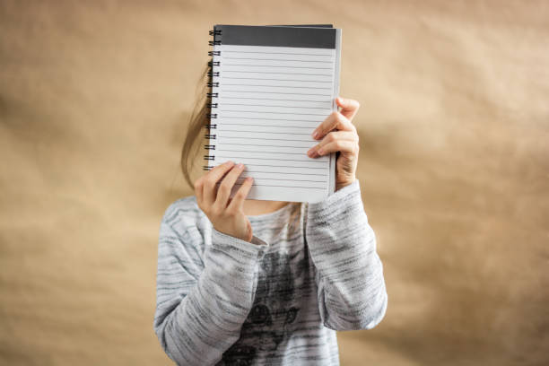istock Front view of unrecognizable person covering her face whit blank paper 1296558541