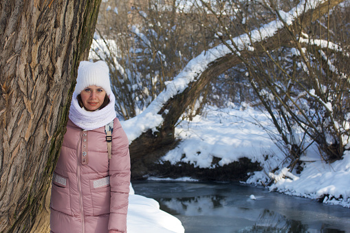 Woman in winter clothes on a walk in the park. A river flows nearby. There is a lot of snow around.
