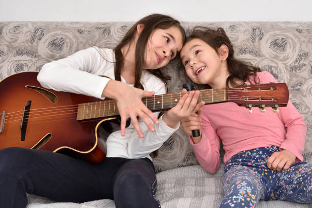 istock Two sisters with a microphone and the guitar sitting on the sofa and singing 1296560190