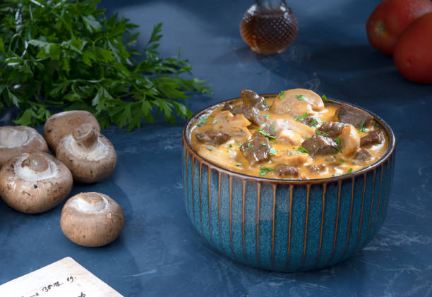Traditional beef stroganoff with cream of champignon mushrooms in a blue bowl with its ingredients. stock photo