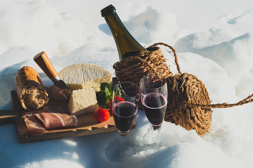 Romantic picnic with Lambrusco cheese baguette and ham on snow. Traditional Italian food and drink in sunny winter day.