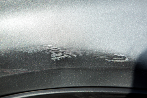 damaged fender of a car is scratched due to an accident, closeup metal texture with damages after crash.