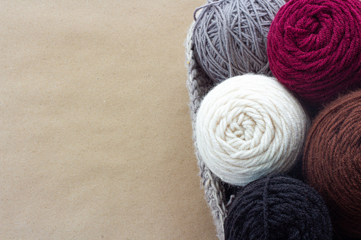 a knitted or crochet basket is full of white, burgundy, gray, brown and black yarn rolls and balls for doing crafting projects