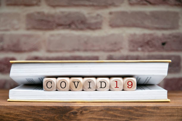 istock Covid 19 word written on wooden blocks between book pages on a shelf. 1296576148