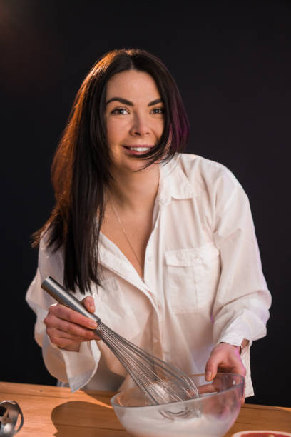istock Young smiling female whisking raw eggs in bowl, cooking breakfast. 1296576911